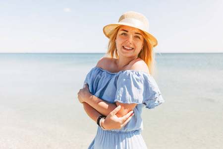 美丽的年轻快乐女人的肖像，戴着草帽，穿着蓝色的裙子，背景是大海