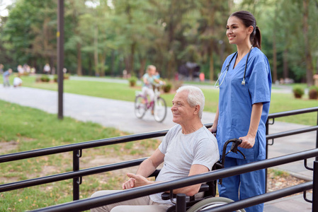 一个坐在轮椅上的老人和一个护士沿着公园的桥漫步
