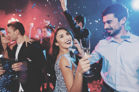 年轻人在新年晚会上玩得很开心。在前景, 一对夫妇在他们手中的眼镜跳舞