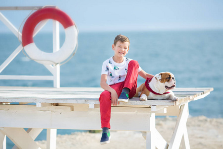 英俊的男孩青少年 happyly 花时间与他的朋友斗牛犬在海边的孩子狗控股玩两个海星接近生活浮标穿红色长裤拖鞋和 tshirt