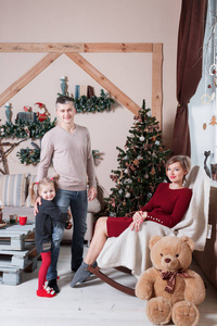 在圣诞节早上看着照相机的年轻友好家庭的画像。父亲 母亲和女儿