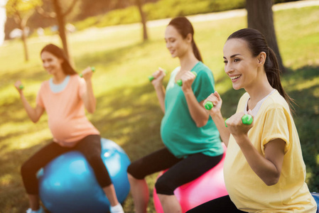 怀孕瑜伽三孕妇在公园内从事健身。他们坐在球的瑜伽