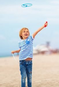 愉快的逗人喜爱的小男孩, 孩子有乐趣在沙滩, 玩休闲活动游戏与螺旋桨玩具