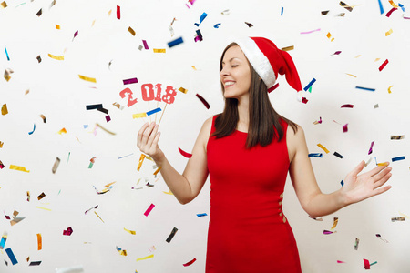 美丽的白种人年轻快乐的女人与健康的皮肤和迷人的笑容在红色的礼服和圣诞帽持有卡号码2018白色背景。孤立的圣诞老人女孩。新年假期概