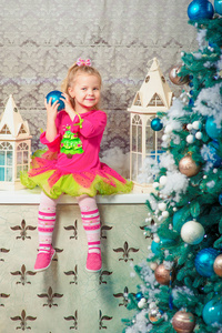 金发可爱的小女孩坐着微笑，几乎装饰圣诞树和新年礼物