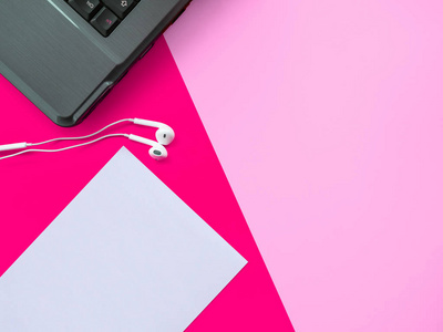 粉红色背景的耳机笔记本电脑和空白纸张