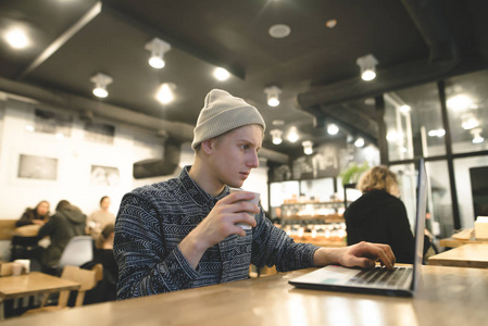 一个年轻的自由职业者在一个郁郁葱葱的咖啡馆和饮料咖啡的笔记本电脑工作。咖啡馆里的一台电脑的时髦学生