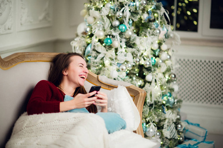 年轻女人作为她 liyng 沙发在家里的圣诞树前签出她手机上的短信