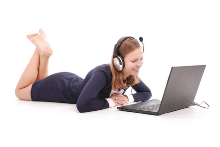 漂亮的年轻十几岁的女孩躺在地上的耳机与笔记本电脑