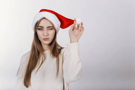 年轻的欧洲女孩对着镜头眨眼。 圣诞老人帽子里的模特。 圣诞节。 复制空间。 广告的地方。