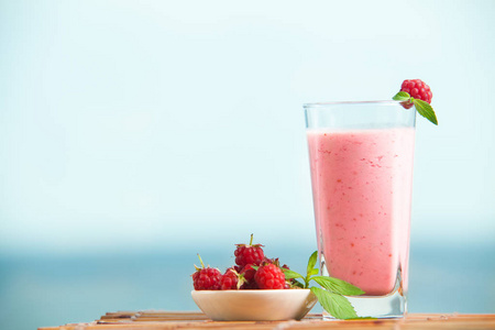 覆盆子奶昔与薄荷在玻璃站在木桌上。 夏季新鲜浆果饮料中的健康饮料。