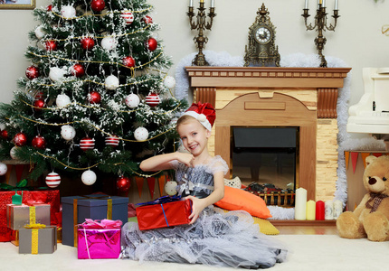 小女孩坐在圣诞树旁与一个大礼物