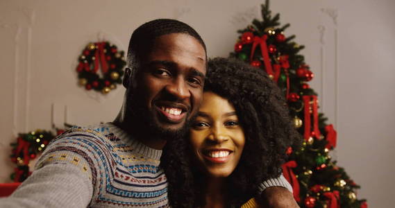 亲密的年轻幸福的非洲裔美国人夫妇 videochatting 和显示在一个圣诞树背景拇指。室内.肖像.pov