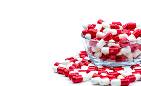 红色, 白色的抗生素胶囊药丸在玻璃碗和一些白色背景与复制空间。耐药性概念。合理和全球医疗保健概念的抗生素用药