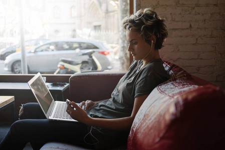 年轻的商务女性坐在一家现代化的咖啡店里，用笔记本电脑打字电子邮件。 自由职业者女孩正在与客户在线沟通，同时访问现代合作空间。