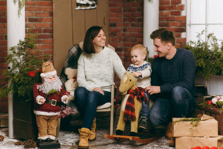 年轻快乐的父母带着一个可爱的小男孩在摇椅上, 穿着毛衣在装修的新年房里与圣诞老人在家里。圣诞节好心情。生活方式, 家庭和假日20