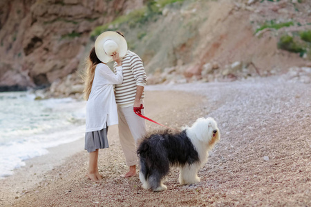 整整一对年轻夫妇站在沙滩上和毛茸茸的狗一起亲吻，躲在帽子后面
