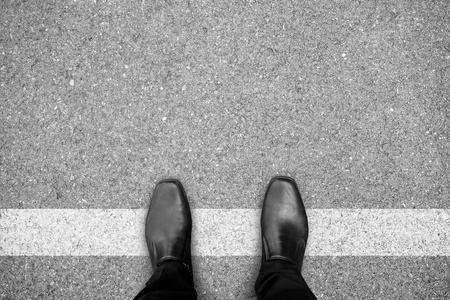 穿黑鞋的商人站在白线上。 禁止和限制。 越过边界。 想得不一样。
