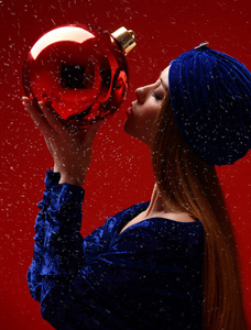 年轻美丽的时尚女性的肖像在蓝色的时尚冬季礼服和帽子接吻臭虫圣诞装饰球