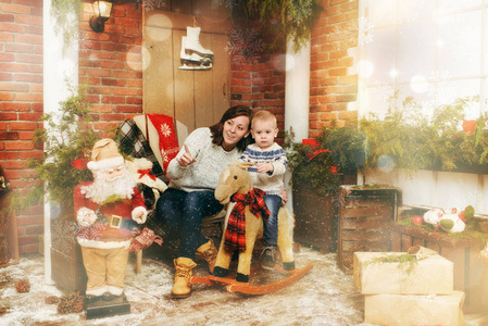 年轻快乐的母亲带着小儿子在装饰着的新年房里和圣诞老人在家里。圣诞节好心情。生活方式, 家庭和假日2018概念。神奇亮点散效果