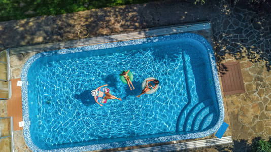 高空俯瞰游泳池中的家庭，从上面快乐的母亲和孩子们在充气环形甜甜圈上游泳，在家庭度假中在水中享受乐趣。