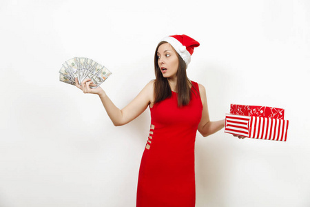 年轻的 disconfused 沮丧的女人在红色的礼服和圣诞帽持有礼品盒和的白色背景。礼物和现金孤立的圣诞老人女孩。新年假期