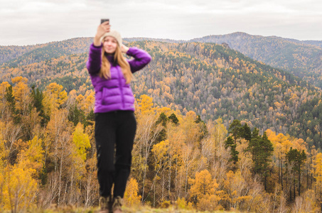 一个穿着紫丁香夹克的女孩在一座山上做一个萨尔菲，在阴天的自由空间里观看山脉和秋天的森林。