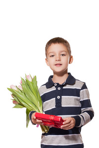 工作室拍摄的可爱的小男孩穿着格子衬衫站在白色的工作室背景上，手里拿着粉红色的郁金香花束和红色的礼品盒