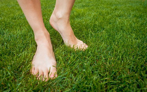 女人的脚在绿色的草坪上。