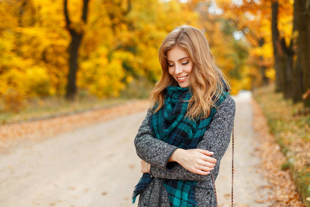 美丽的年轻快乐的女人在秋季公园的时尚大衣摆姿势