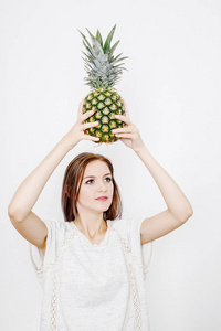 女孩拿着菠萝。 带菠萝的年轻女人。 水果和蔬菜在他们手中。 头上的菠萝。