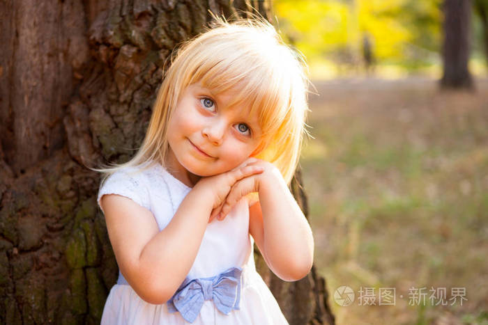 可爱的小女孩靠在大树上,微笑着的童年概念