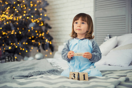 情绪微笑的小女孩坐在睡衣与圣诞礼物附近的新年树和玩雪球