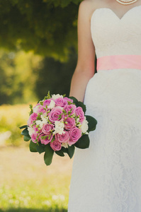 婚礼结束后，新娘在阳光公园里捧着一束美丽的粉红色和白色的花