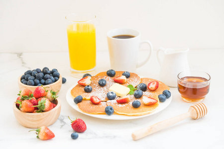 健康早餐，白石桌背景上有薄饼蓝莓和草莓水果黑咖啡牛奶和橙汁