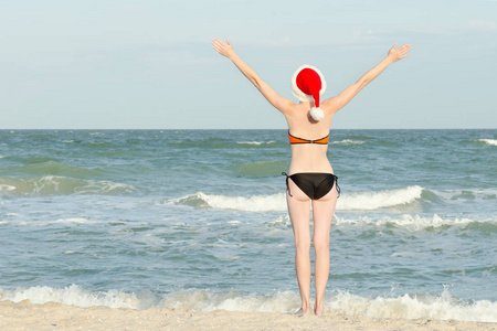 女孩在海滩在圣诞老人帽子。举手。后视图