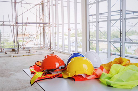 白色橙色黄色蓝色安全帽，工地办公桌上有反光衣，脚手架背景工程师安全工业和建筑概念