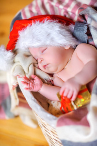 戴着圣诞老人帽子的漂亮宝宝躺在篮子里，抱着一个带礼物的小盒子睡着了