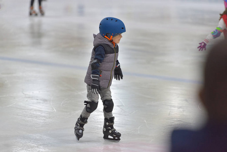 可爱的小男孩在冬季的衣服在溜冰场滑冰的保护
