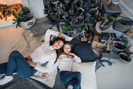 美丽幸福的家庭母亲和女儿的礼物围绕圣诞树在地板上一起在家里