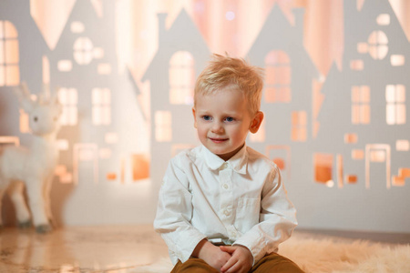 可爱的金发小男孩靠近圣诞玩具纸房子。