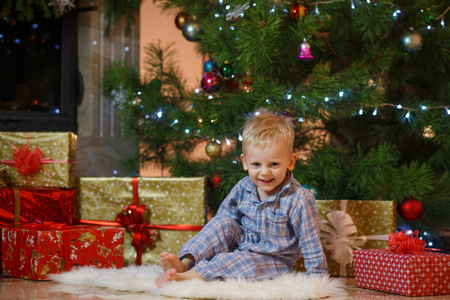 可爱的金发小男孩靠近壁炉和礼物在圣诞树下。