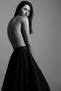 女性美的概念。时尚的年轻女孩的肖像黑色波尔卡点裙和运动鞋摆在灰色背景。完美的发型和皮肤时尚风格。演播室射击。黑白 单色 照片