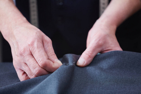 特写不可辨认的熟练裁缝在工作室工作双手缝制织物，同时在桌子上缝制衣服
