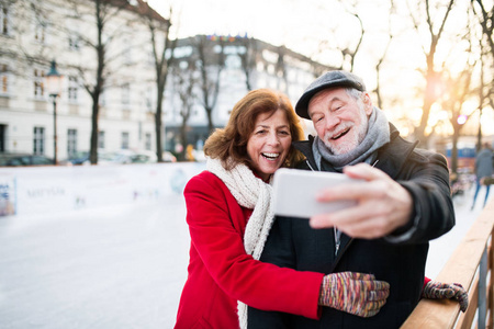 在冬天的城市散步的资深夫妇与智能手机