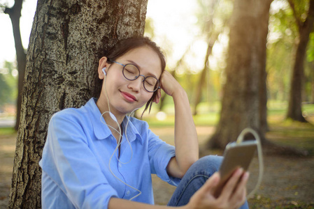 亚洲妇女听音乐从智能手机下的树