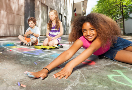 一群孩子在院子里用粉笔画画，漂亮的卷曲非洲女孩伸出手来