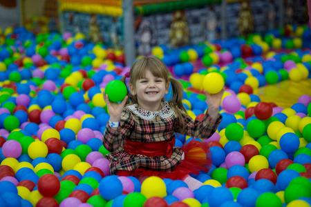 快乐的小女孩穿着红色的裙子在游泳池里玩五颜六色的塑料球。 有趣的孩子在室内玩得很开心。