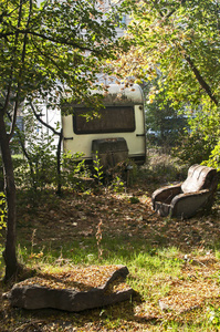 古老的老式废弃的Grunge大篷车和破旧的扶手椅，在杂草丛生的地方。