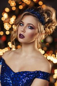 一幅美丽的女孩的肖像，她穿着深蓝色的连衣裙，戴着亮片，在模糊的圣诞树前摆着粉红色的礼品